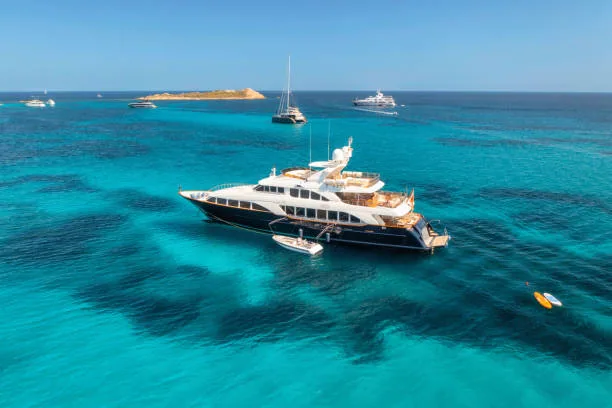 Aerial view of luxury yacht on blue sea at sunny day in summer. Sardinia, Italy. Aerial view of speed boats, yachts, sea lagoon, shore, transparent water, sky. Top view from drone. Tropical seascape